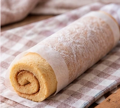 Génoise encore tiède roulée avec le papier cuisson pour prendre sa forme en spirale